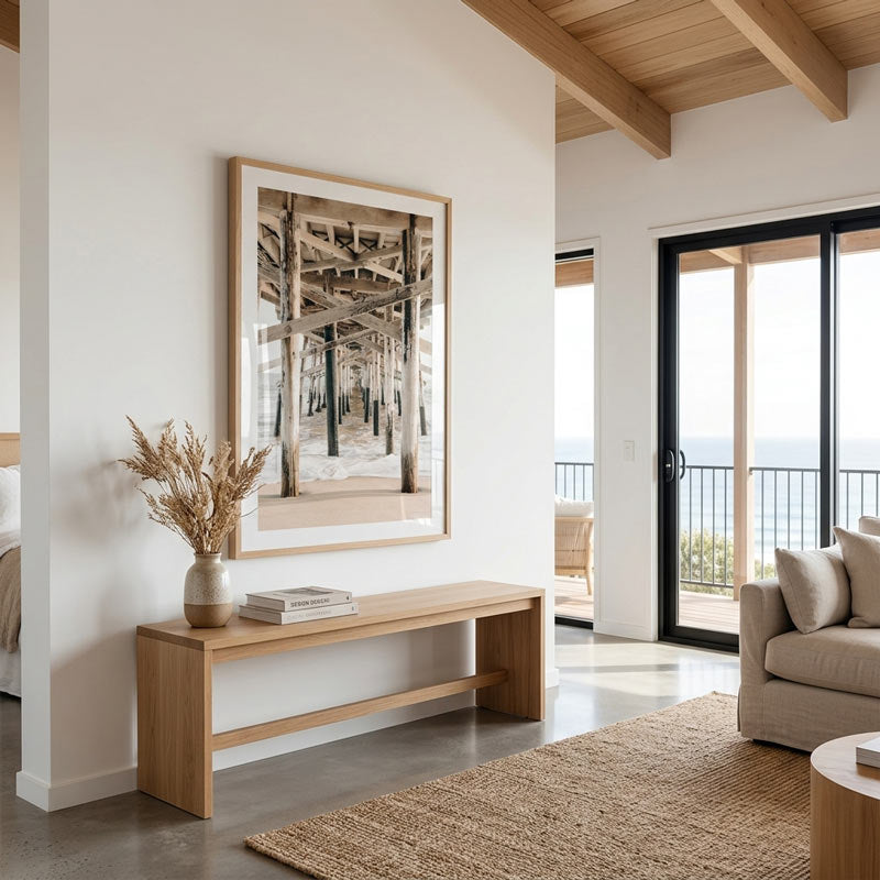 Modern living room with wooden bench, framed artwork, and a view of the ocean.