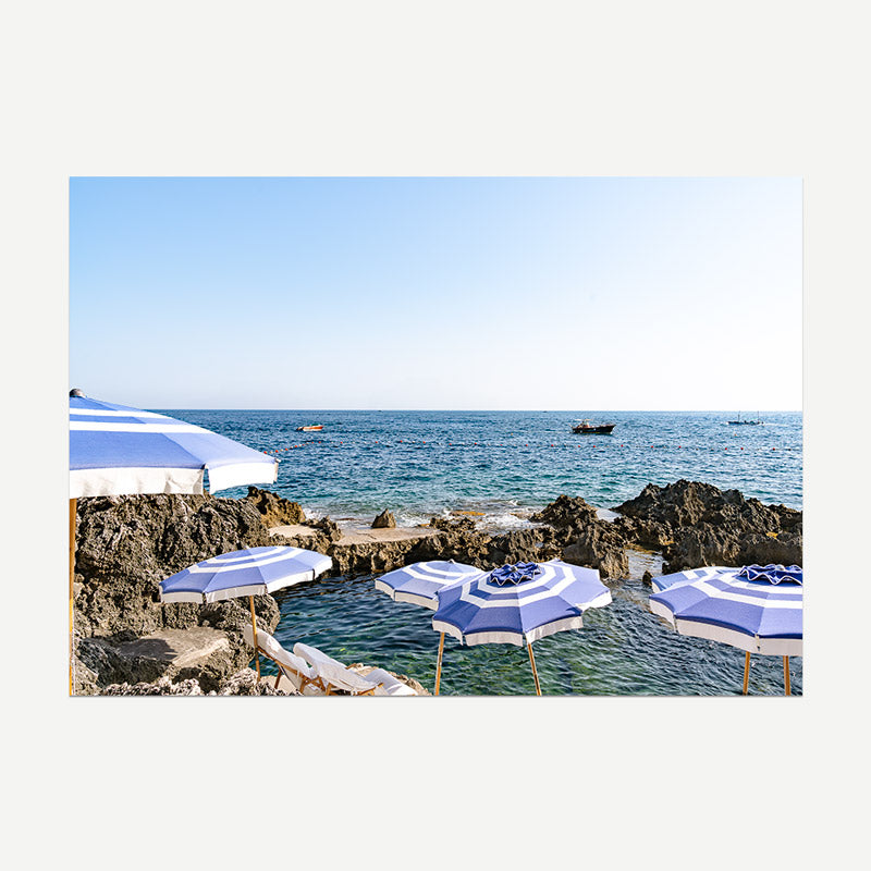 Blue and white striped umbrellas on a rocky beach with ocean and sky in the background