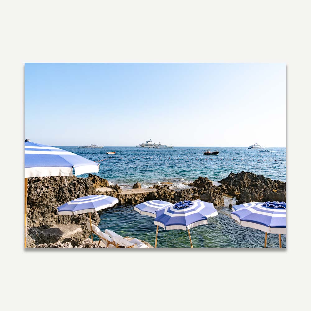La Fontelina Beach Club in Capri featuring blue and white beach umbrellas casting serene silhouettes in the late afternoon sun.