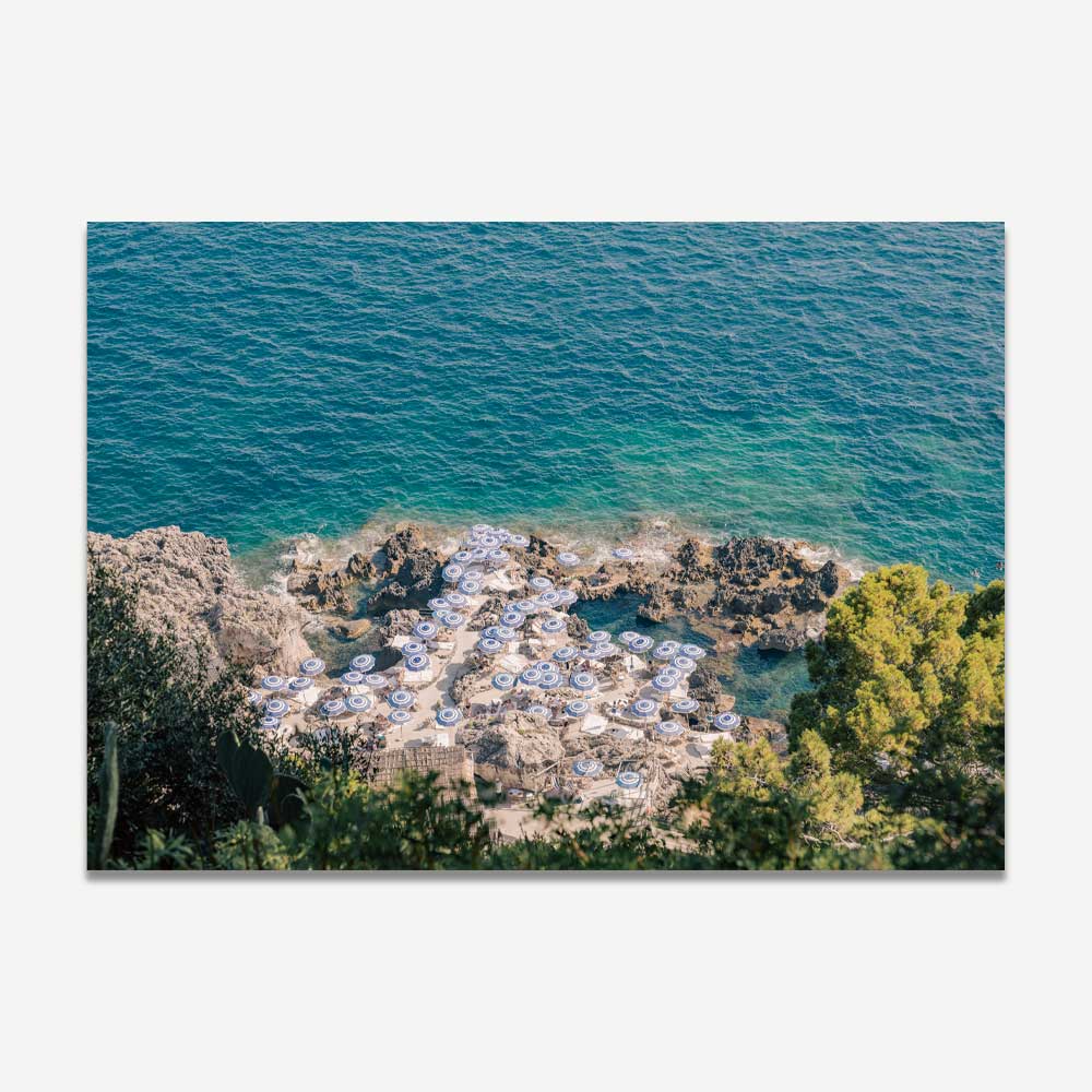 La Fontelina Beach Club in Capri, with vibrant blue and white beach umbrellas on rocky Mediterranean shores under a sun-soaked summer sky, evoking coastal beauty and Italian elegance.