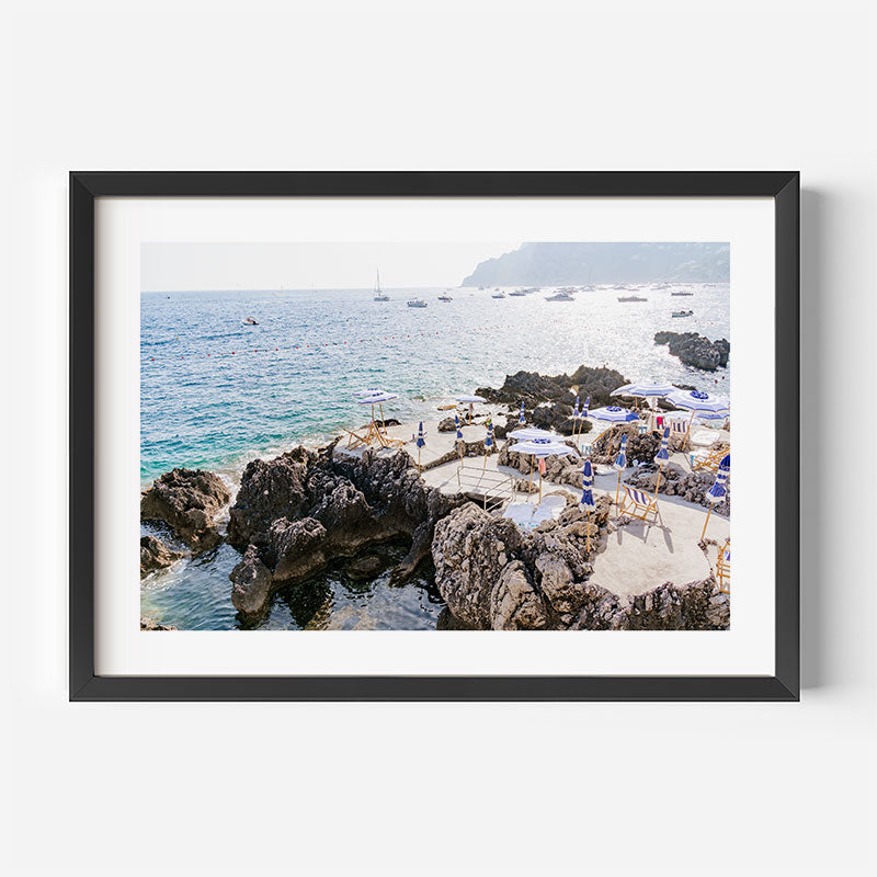 Framed photograph of a rocky beach with people and boats on a clear day.