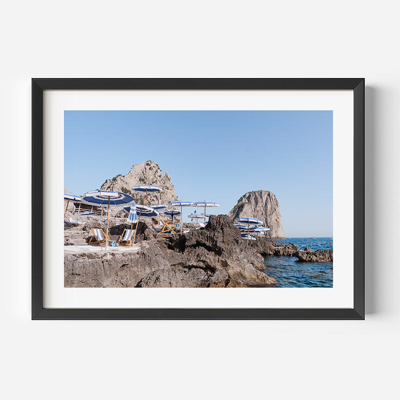 Framed photograph of a rocky coastal scene with lounge chairs and umbrellas.