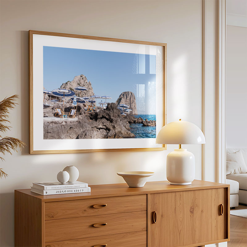 Framed artwork of a coastal scene on a wall above a wooden sideboard with decor items.