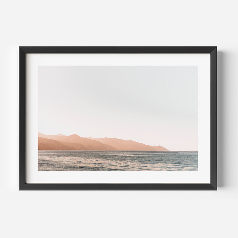 Framed artwork of a landscape with mountains and water on a white wall