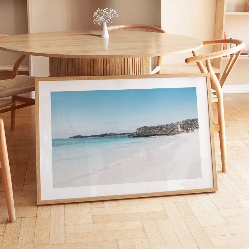 Framed beach photo on a wooden floor with a dining table and chairs in the background