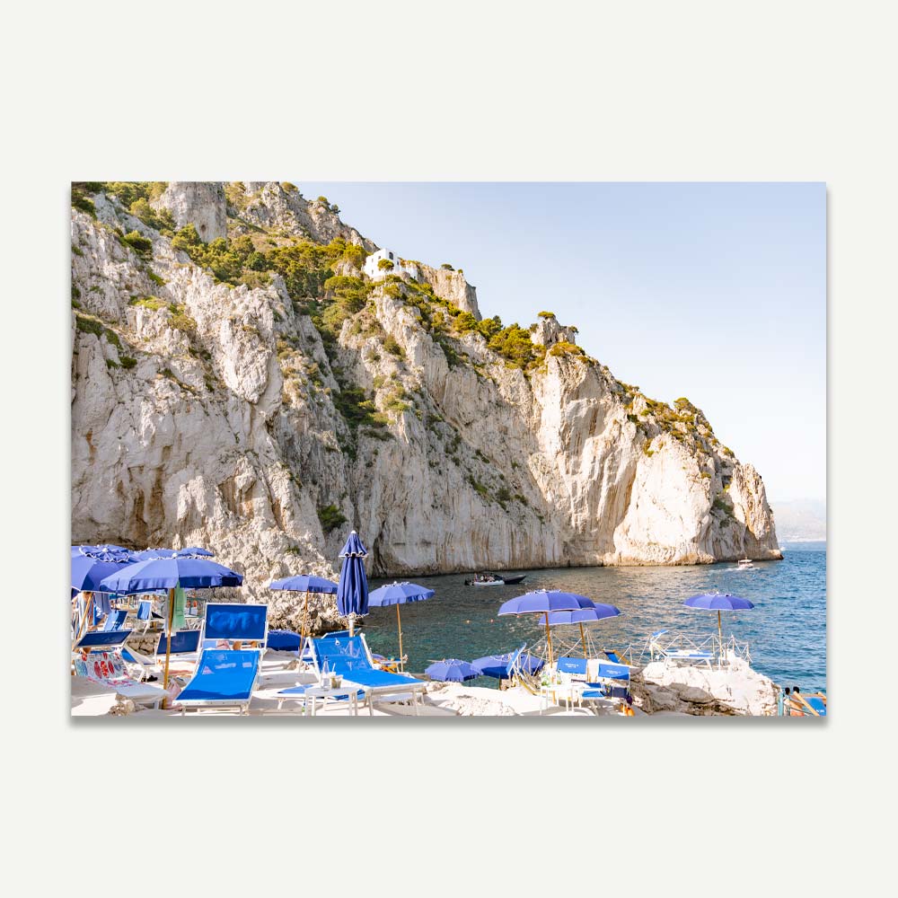 DA LUIGI AI FARAGLIONI Beach Club in Capri with iconic blue beach umbrellas against a secluded cove at sunset, evoking tranquility and Mediterranean luxury.