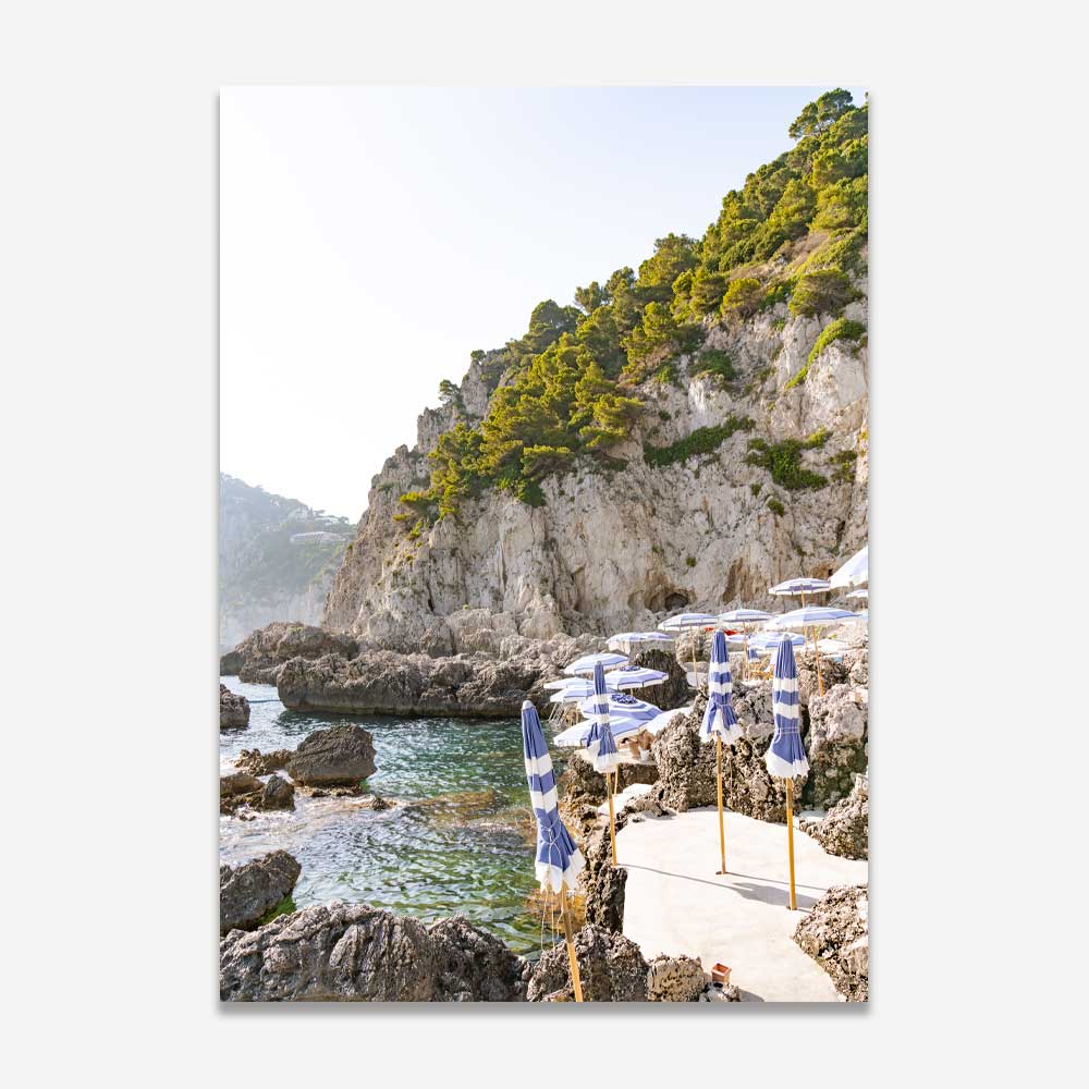 La Fontelina Beach Club in Capri, with vibrant blue and white beach umbrellas on rocky Mediterranean shores under a sun-soaked summer sky, evoking coastal beauty and Italian elegance.