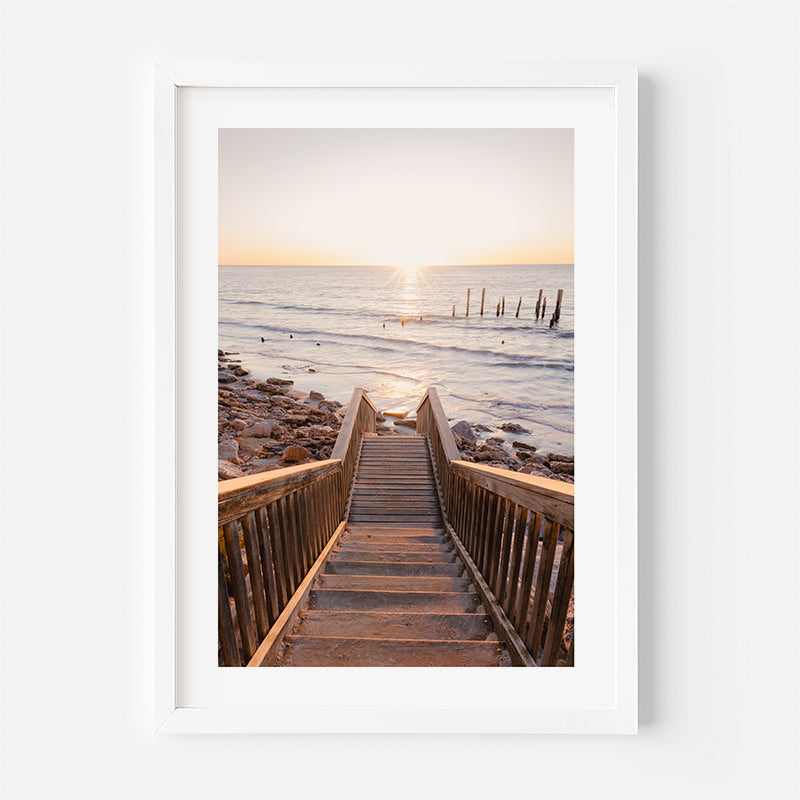 Wooden staircase leading to a beach with a sunset over the ocean.