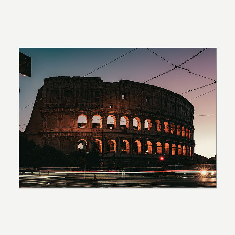 A rectangular wall art print showing the Colosseum in Rome at dusk, with the illuminated ancient structure against a purple and blue twilight sky. The print is photographed hanging or mounted against a plain light gray wall.