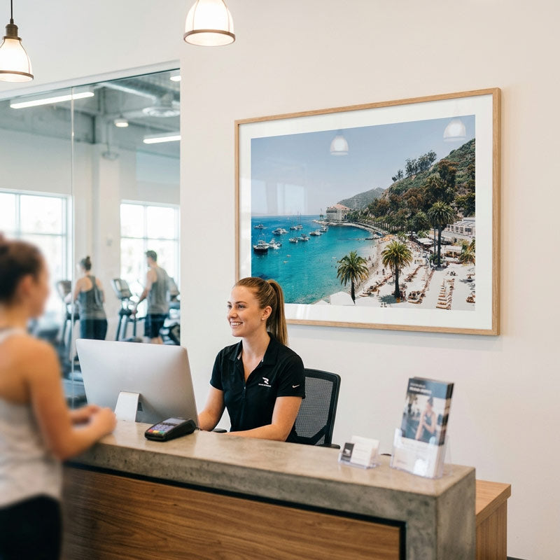 Woman at a reception desk with a framed picture of a beach scene on the wall.