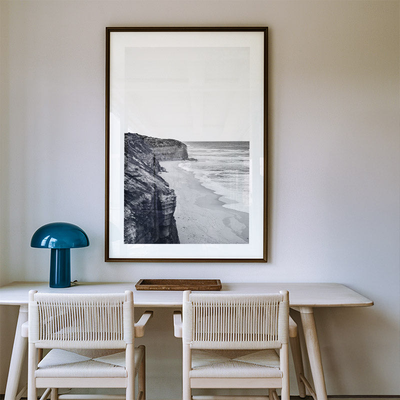 Dining area with a framed black and white landscape, blue lamp, and wooden table.