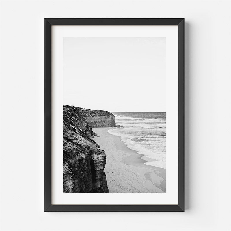 Framed black and white photograph of a beach and cliffs on a white wall