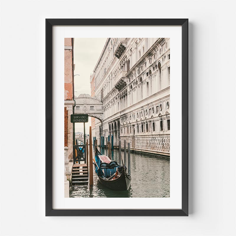 Framed photograph of a gondola on a canal in Venice with a building in the background.