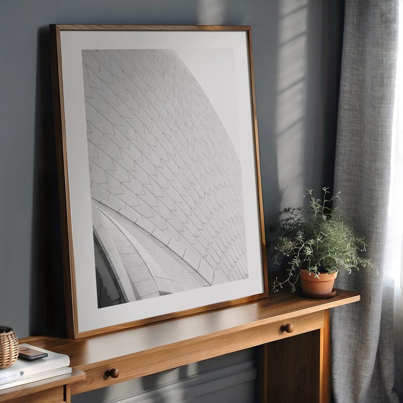 Framed artwork on a wooden console table with a plant against a gray wall.