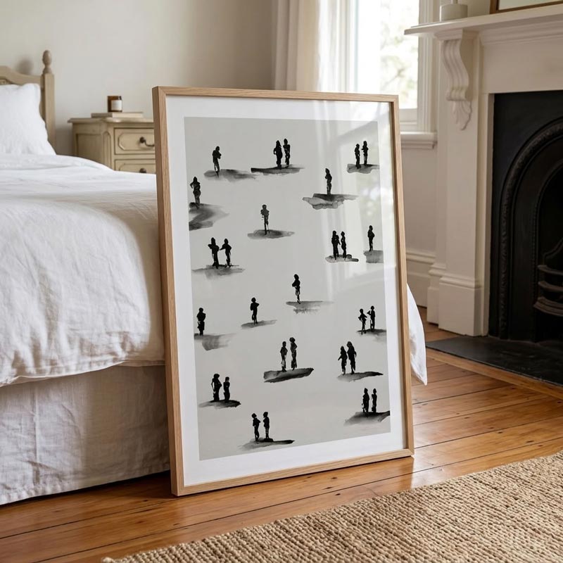 A framed black and white art print featuring minimalist figures standing on surfboards, leaning against a bed in a bright, neutral bedroom with wooden floors and a fireplace.