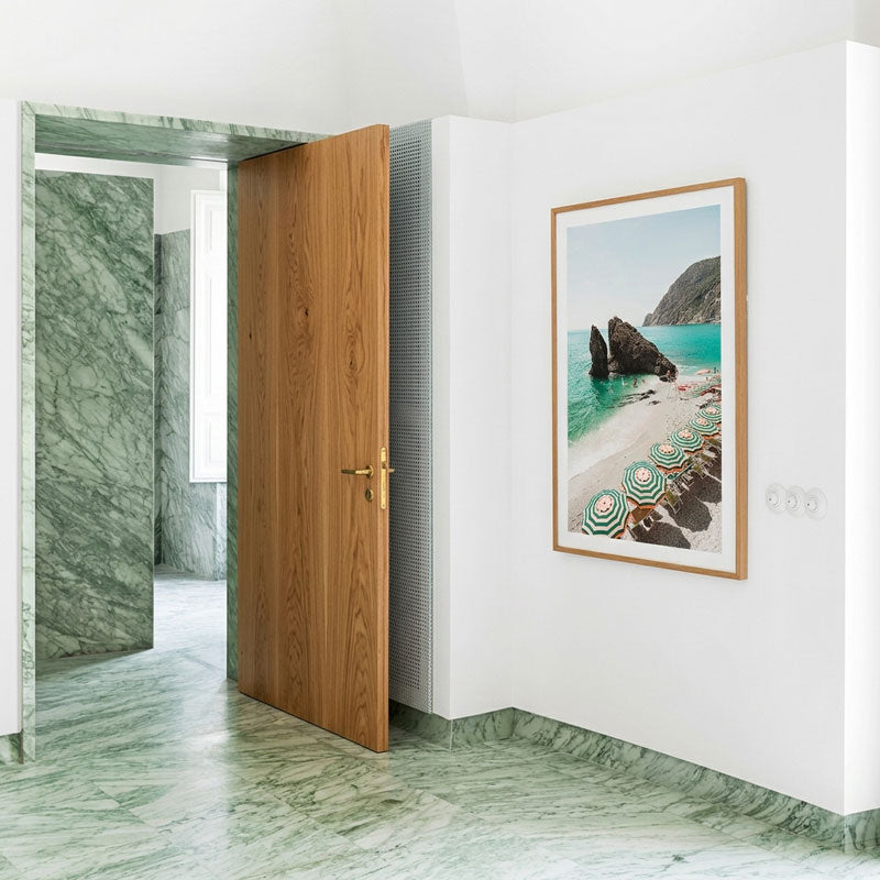 Wooden door in a room with marble walls and floor, framed artwork on the wall.