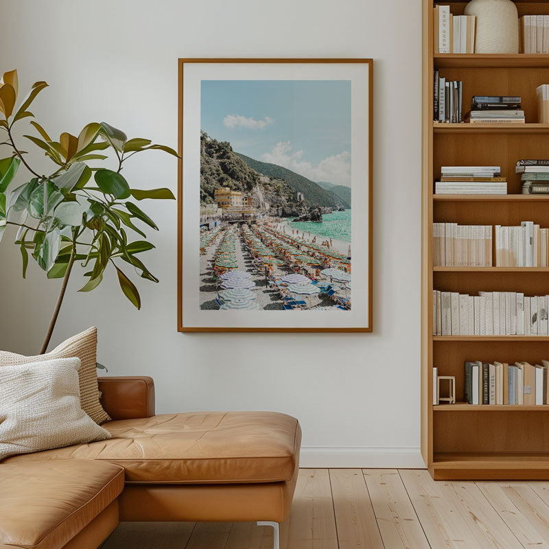 Living room with brown leather sofa, bookshelf, and framed artwork of a coastal scene.