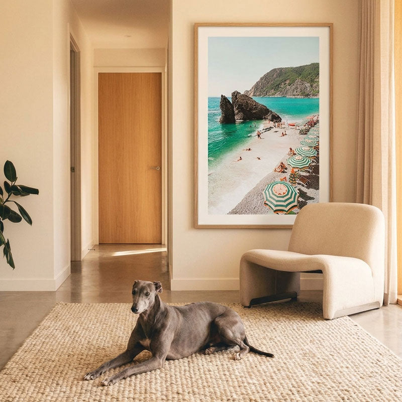 Dog lying on a rug in a room with a chair and a large framed picture of a beach.