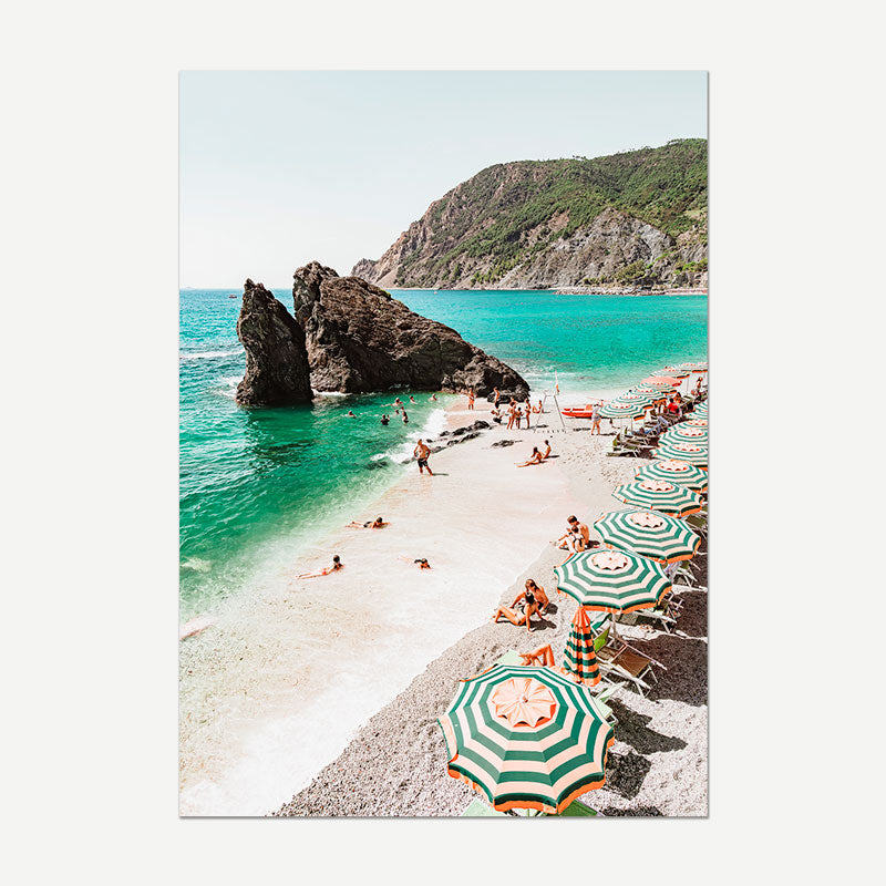 Beach scene with striped umbrellas and people enjoying the sun, surrounded by clear blue water and rocky cliffs.