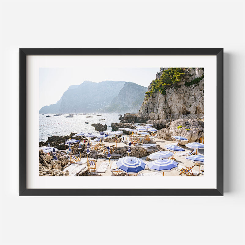 Framed photograph of a rocky beach with umbrellas and mountains in the background