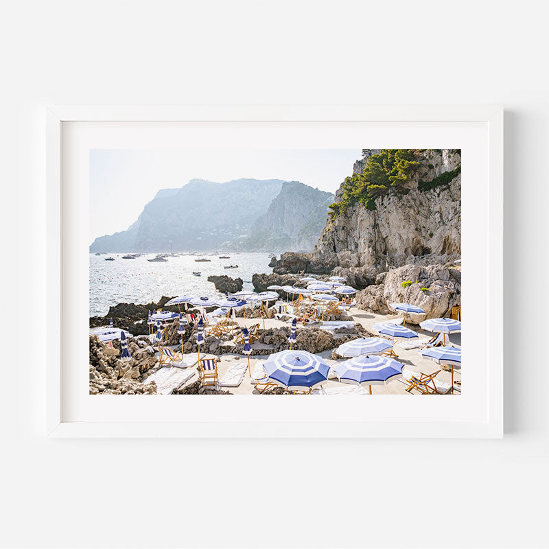 Beach scene with umbrellas and chairs on a rocky shore with mountains in the background