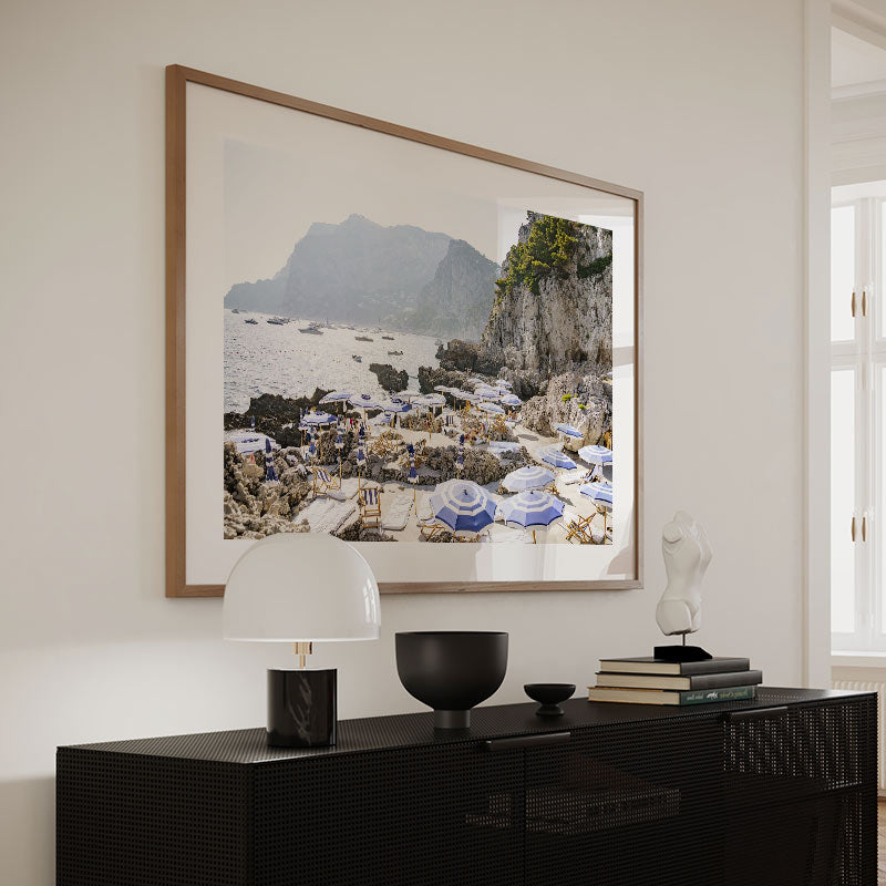 Framed artwork of a coastal scene above a black console table with decorative items.