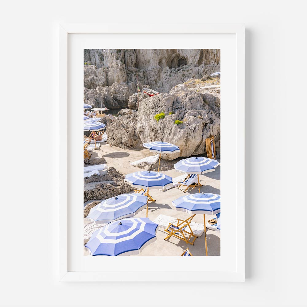 La Fontelina, Capri, Italy: A serene coastal haven adorned with sunbathing chairs and umbrellas, framed by the majestic mountainscape. Perfect for fine art prints, adding a touch of coastal charm to your wall decor.