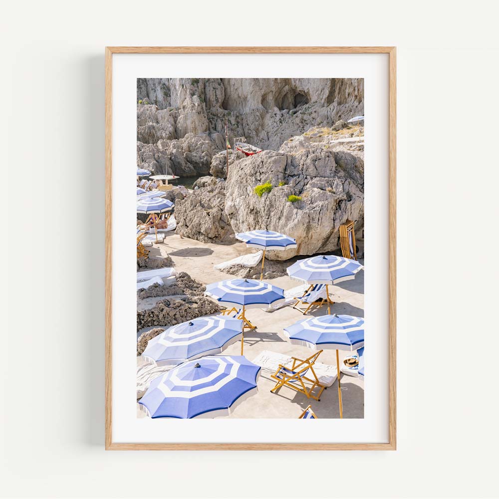 Coastal Elegance: La Fontelina, Capri, Italy, features sunbathing chairs and umbrellas with mountain backdrop, enhancing wall decor.