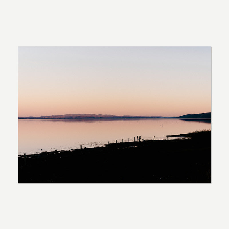 Silhouette of a fence on a beach with a pink and purple sunset over water