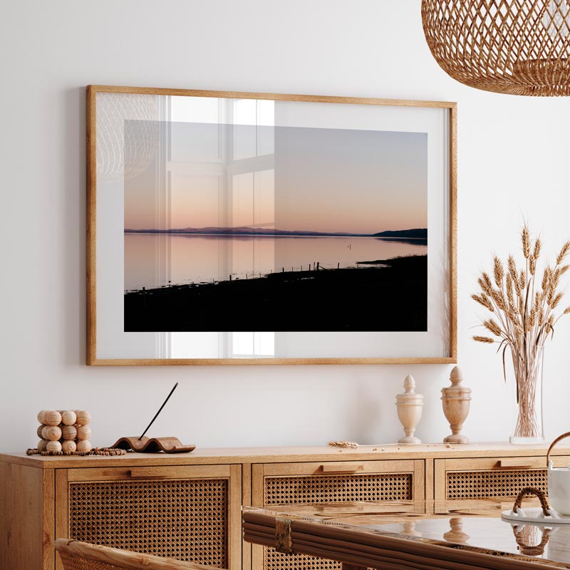 Framed artwork of a landscape with a wooden cabinet and decorative items in a room.