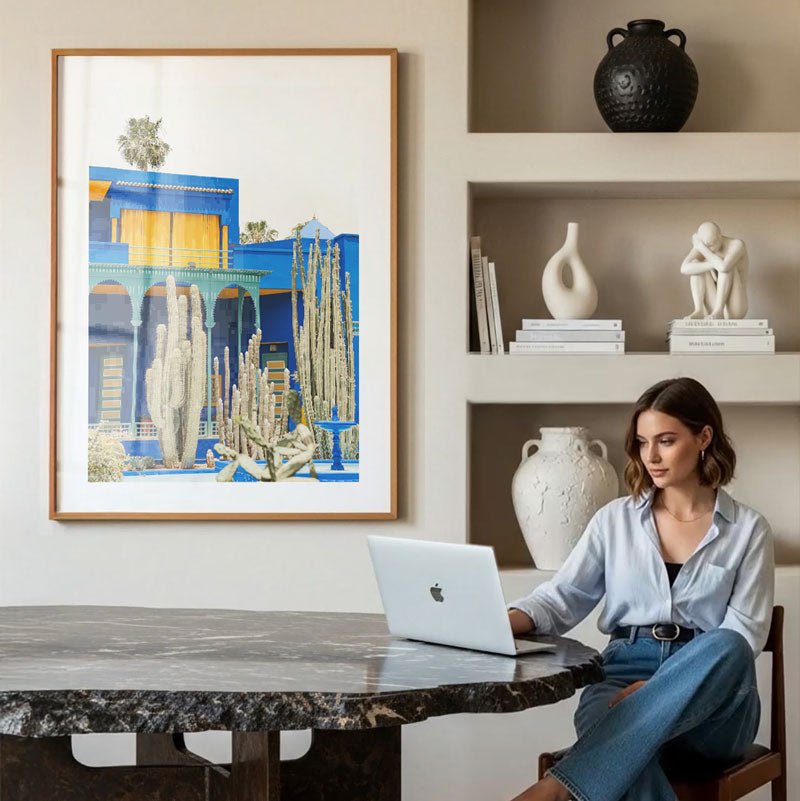 Woman using a laptop at a table with decorative items and a large framed artwork in the background.