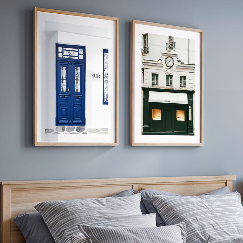 Two framed artworks on a wall above a bed with gray bedding.