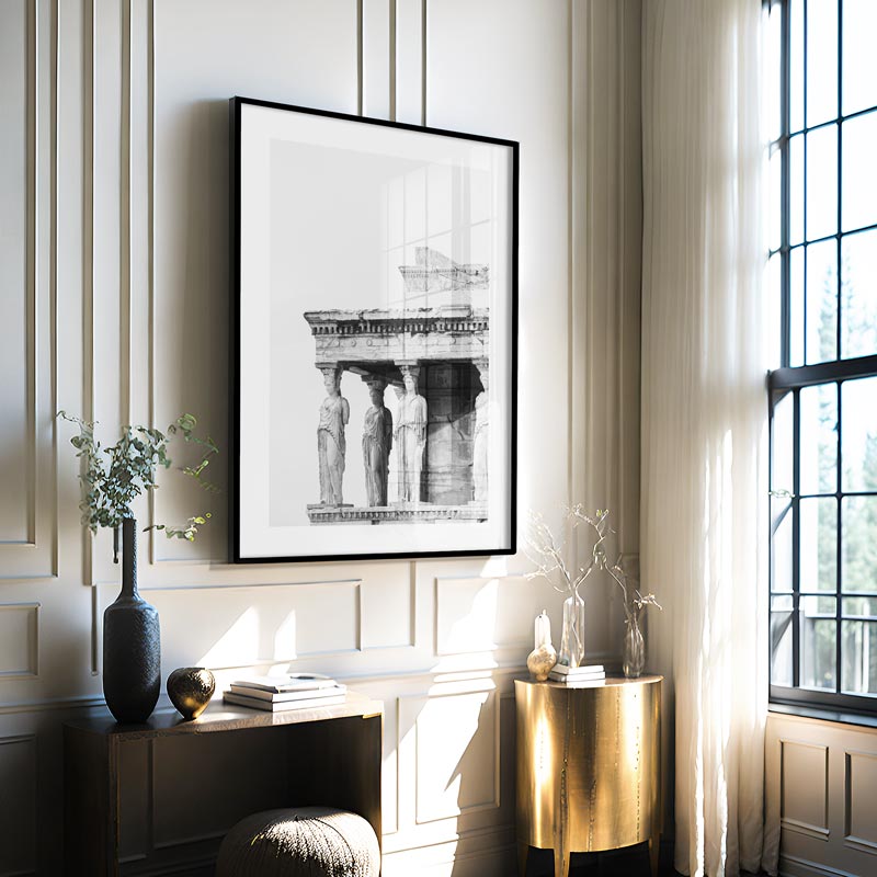 Framed black and white art print on a wall in a stylish room with a window and decorative items.