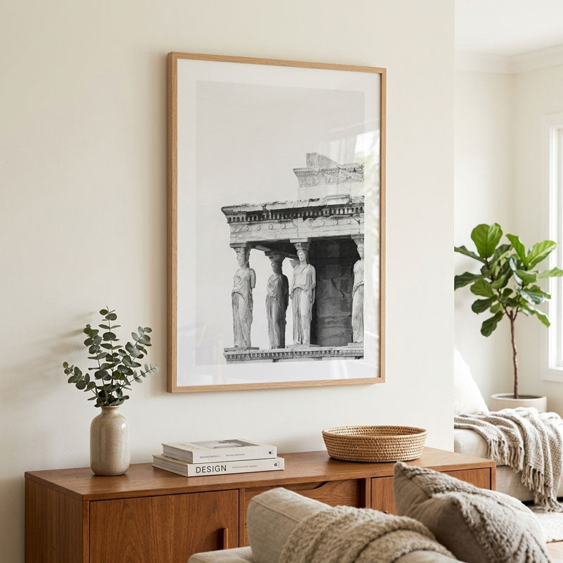 A large framed black and white architectural art print of ancient Greek or Roman columns hangs on a cream wall above a wooden console table in a styled living room.