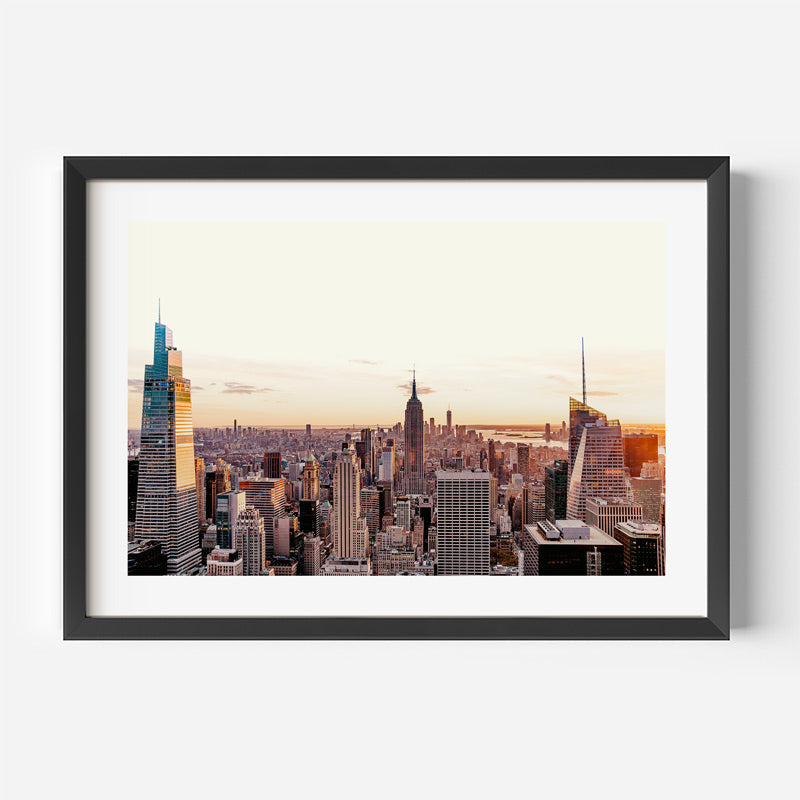 Framed cityscape print of a skyline with sunset, displayed on a white wall.