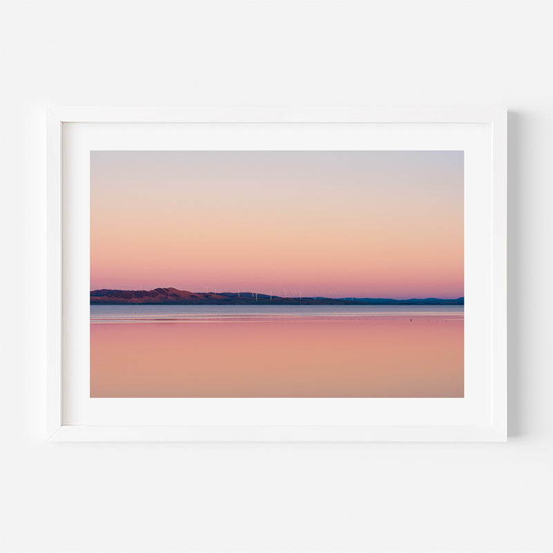 Framed artwork of a landscape with a pink and purple gradient sky over water.