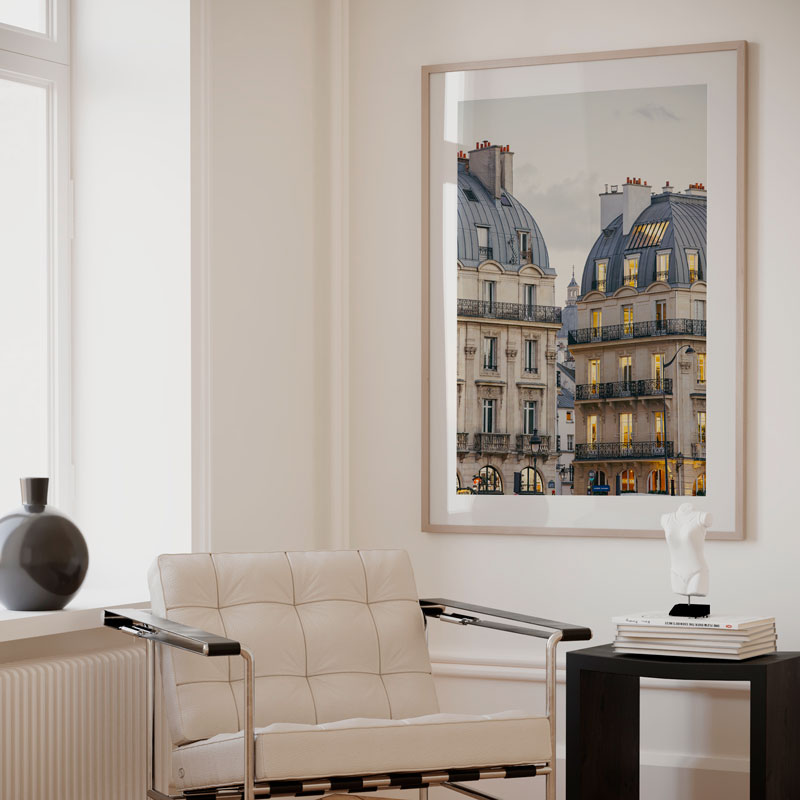 Modern living room with a beige sofa, side table, and framed artwork of city architecture.