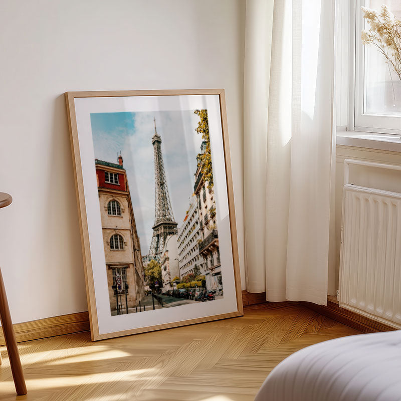 Framed picture of the Eiffel Tower on a wall in a room with a window and radiator.