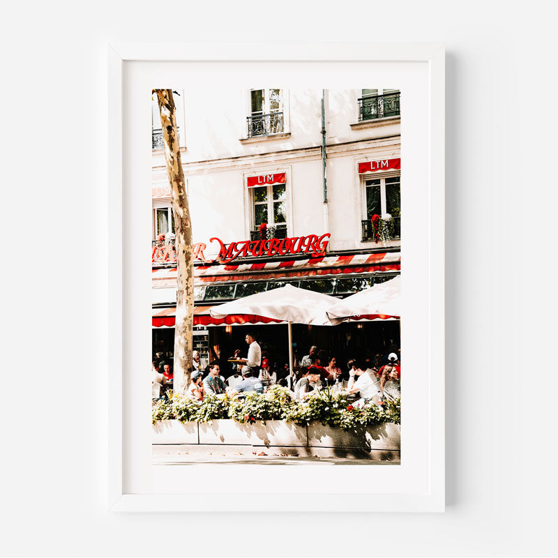 Outdoor cafe scene with people under white umbrellas in front of a building with a red sign.