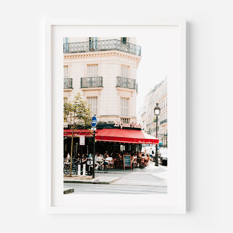 Framed photograph of a street scene with a red awning and people sitting outside a cafe.
