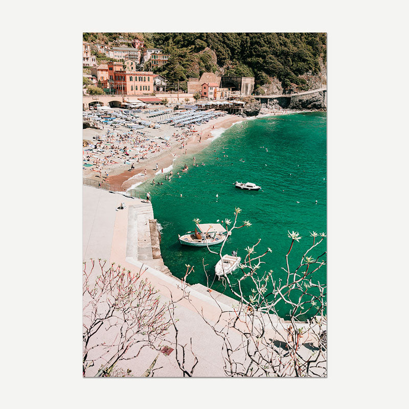 Coastal scene with boats, beach, and buildings on a hillside.