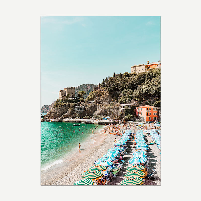 Beach scene with colorful umbrellas and people, surrounded by a coastal town.