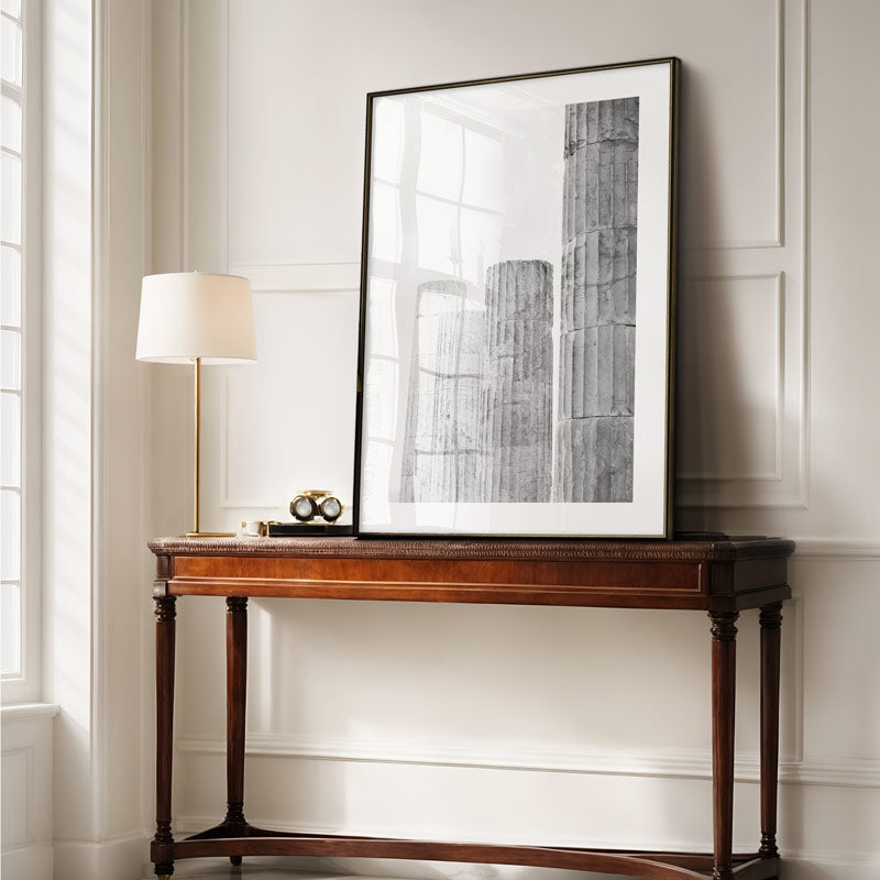 Wooden console table with a framed black and white artwork in a room with neutral walls and a lamp.