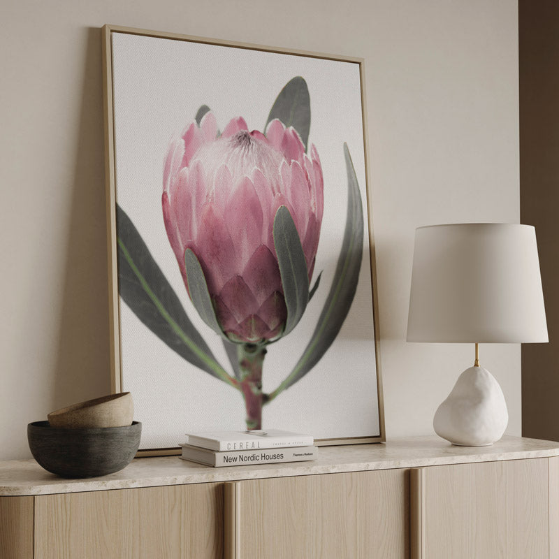 Framed artwork of a pink flower on a wall above a wooden cabinet with decor items.