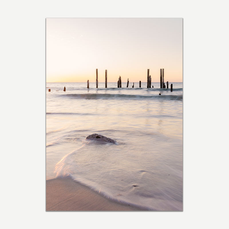 Beach scene with waves and wooden posts at sunset
