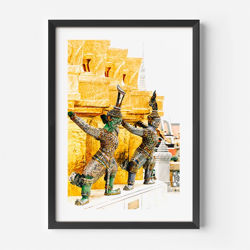 A framed art print featuring three Thai temple guardian statues in green and gold armor against a golden background, presented in a black frame on a white wall.