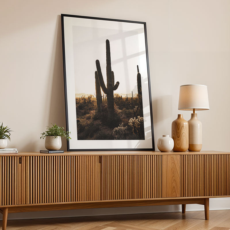 Framed artwork of a cactus on a wooden sideboard with decorative items.