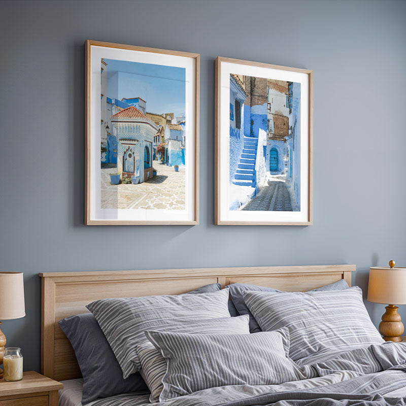 Two framed artworks on a wall above a bed with striped bedding.
