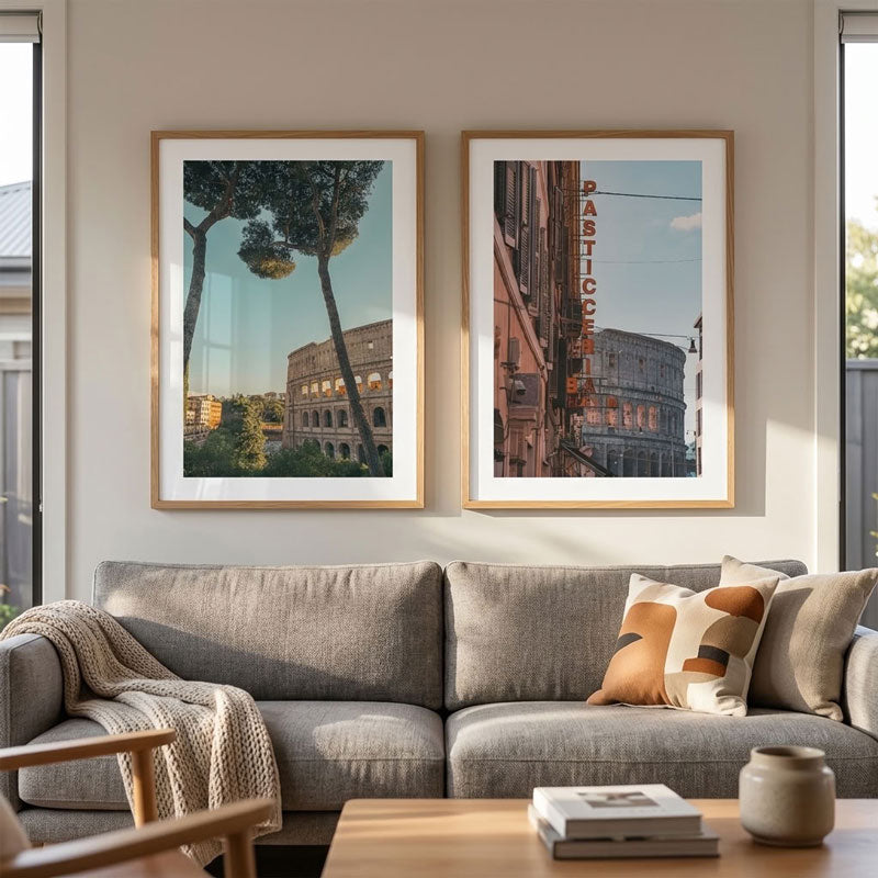 Two framed art prints depicting the Colosseum in Rome hang above a gray fabric sofa in a modern living room setting.