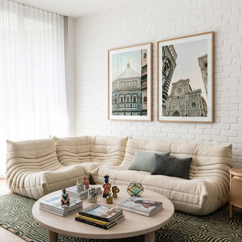 Modern living room with a beige sectional sofa, coffee table, and framed artworks on a white brick wall.